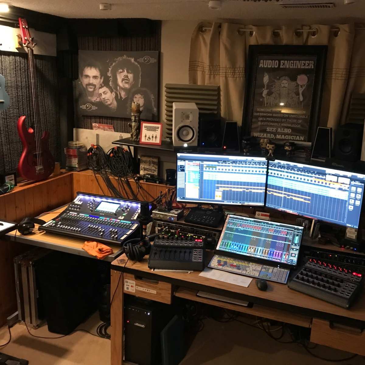 A music recording studio with multiple audio equipment, instruments, and two large computer monitors displaying sound editing software.
