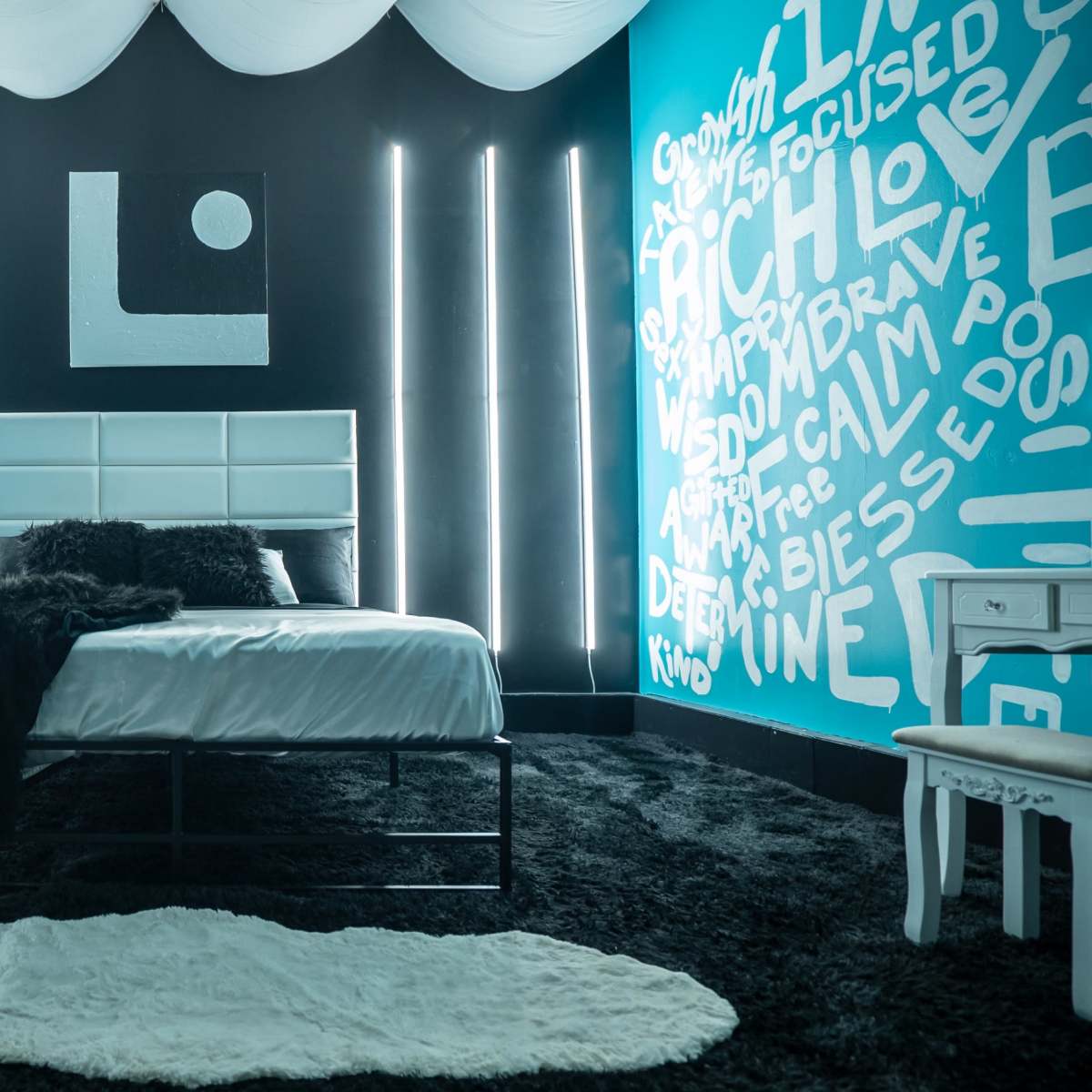 A modern bedroom with a bed covered in white linens, a black shag carpet, and walls painted in contrasting teal and black, featuring decorative lighting and text art.