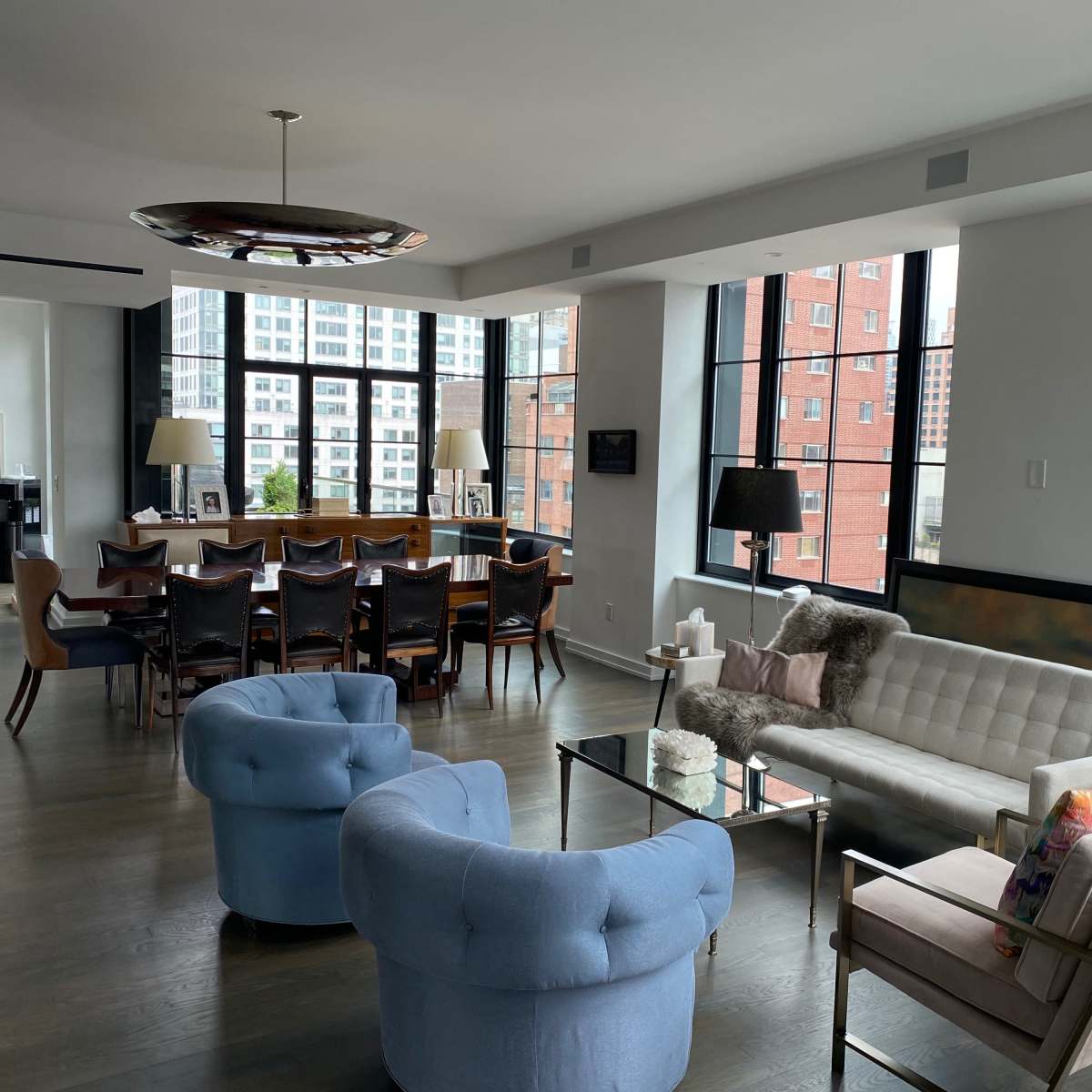 A modern open-concept living area with a dining table, stylish seating, and large windows offering urban views.