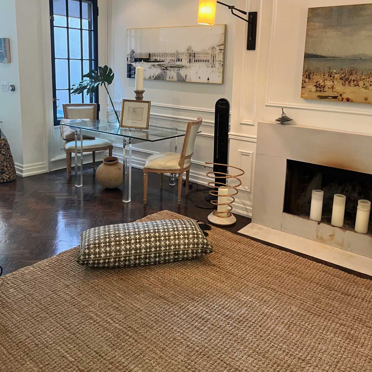 A modern living room with a glass dining table, a wall-mounted lamp, and a fireplace featuring several candles.