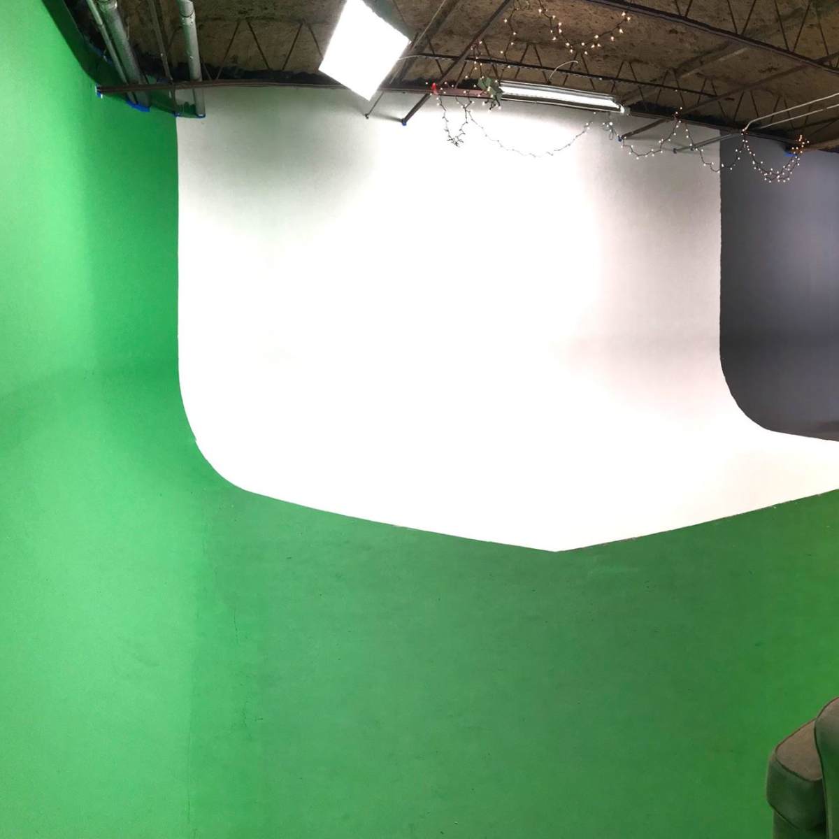 A photography studio with a green, white, and gray backdrop, along with various studio equipment and furniture.