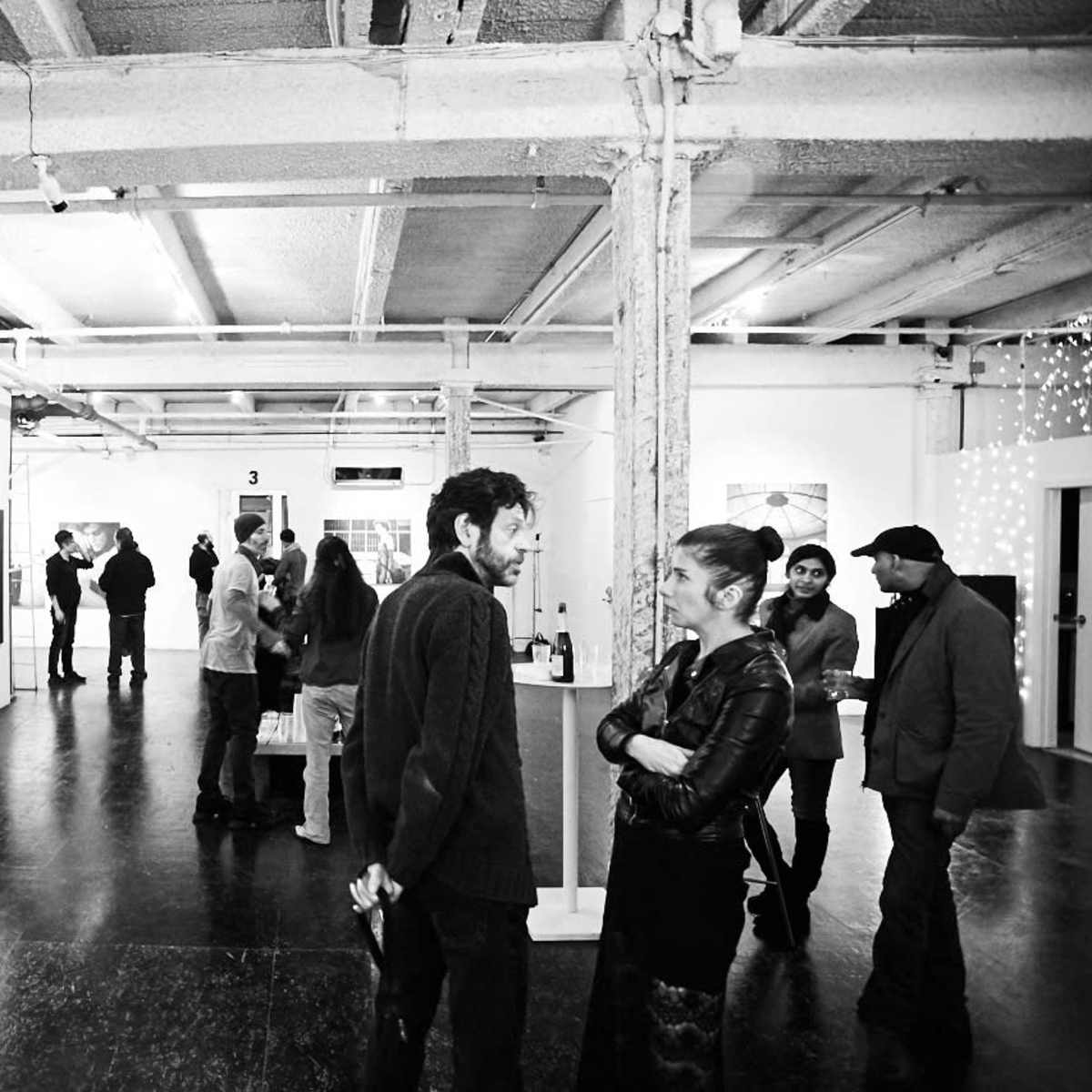 An art gallery showcases several paintings on the walls while guests engage in conversation and explore the space.
