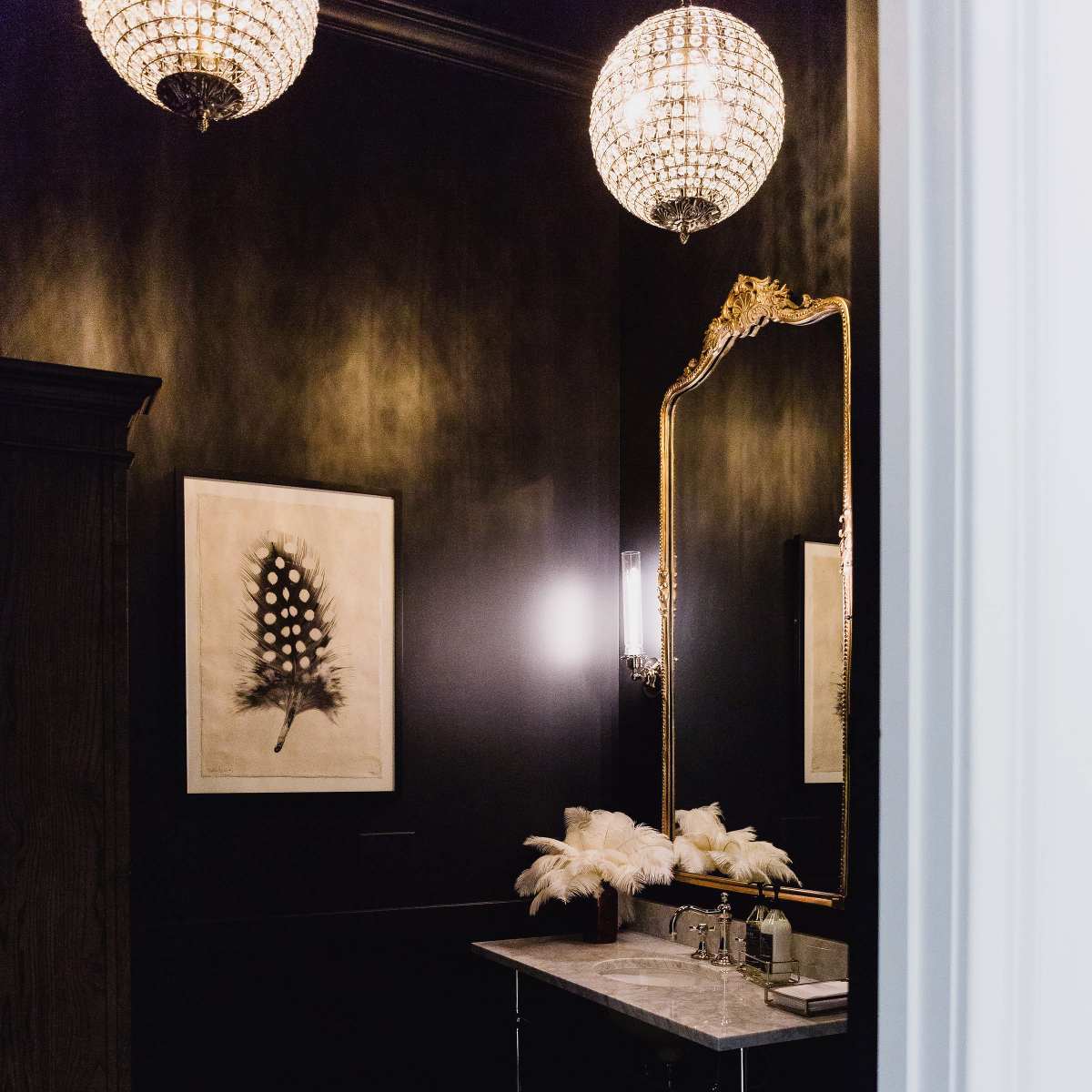 A dimly lit bathroom featuring a marble sink, feather décor, a large mirror, and patterned tile flooring.