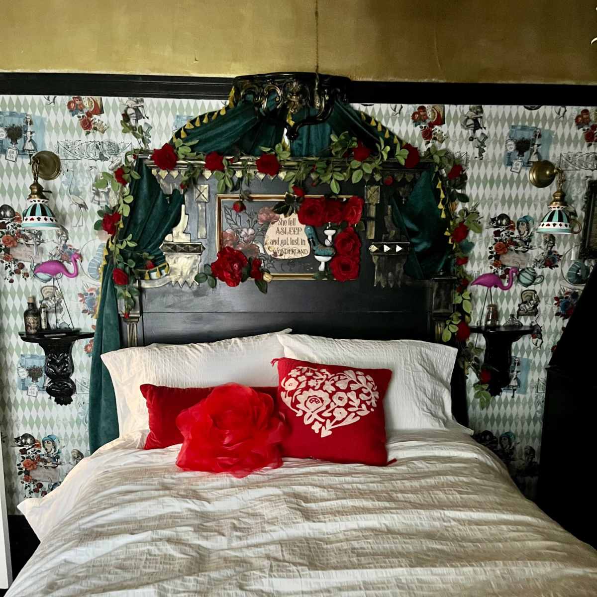 A bed with a decorative black headboard adorned with red roses and greenery, set against patterned wallpaper featuring playful designs.