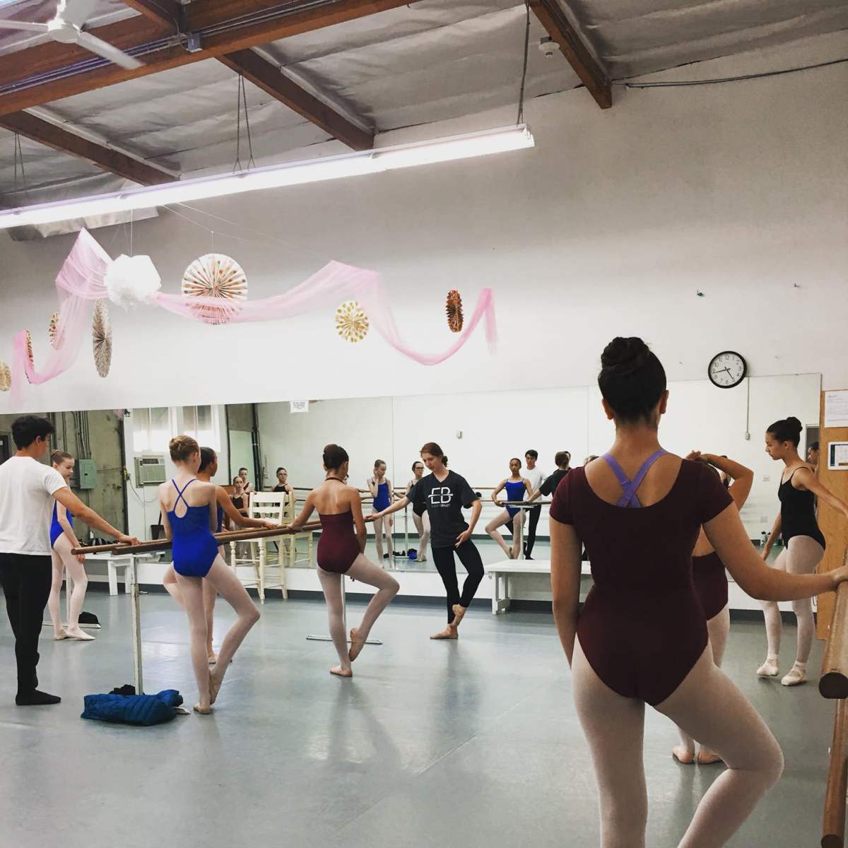 A group of ballet students practices at a dance studio with mirrors and barre equipment.
