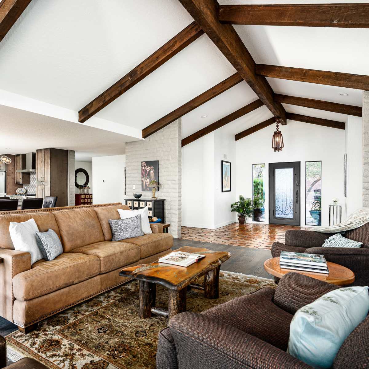 The living room features a combination of a brown leather sofa and two upholstered chairs, with wooden beams overhead and a stone wall.