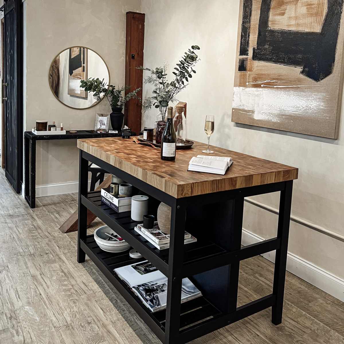 A modern interior space featuring a wood and black metal table with decorative items, a round mirror on the wall, and artwork hung above it.