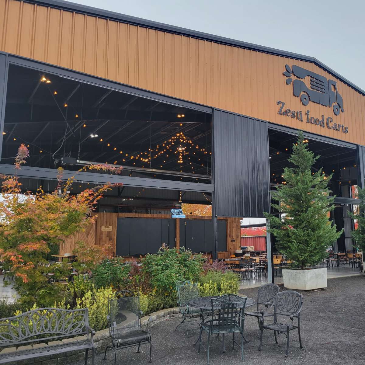 A large food cart area with a covered structure, featuring string lights and outdoor seating surrounded by greenery.