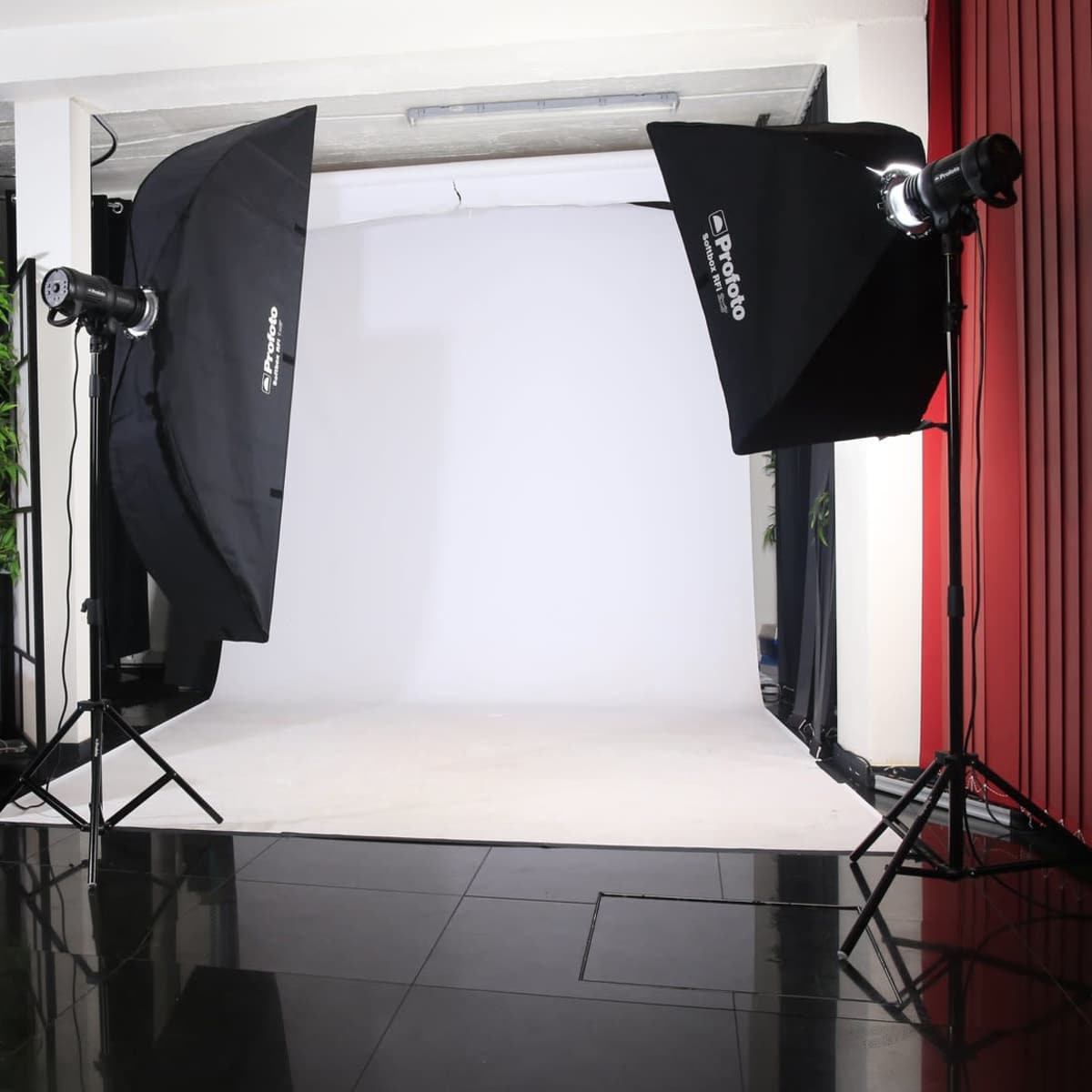 A photography studio with two large softbox lights facing a plain white backdrop, a black floor, and a white couch positioned to the side.