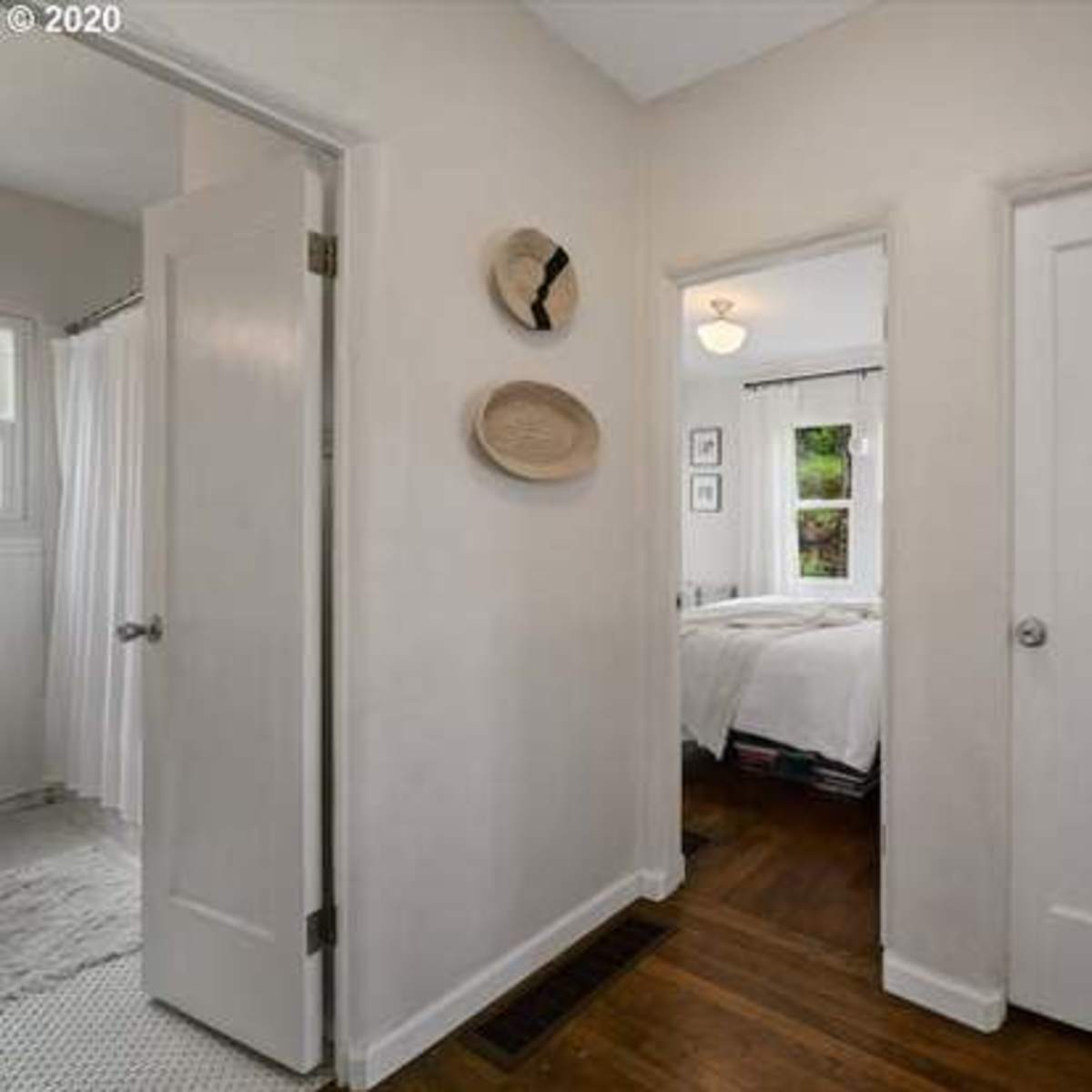 A narrow hallway features two doors leading to adjacent rooms, with wall decor and a light fixture overhead.