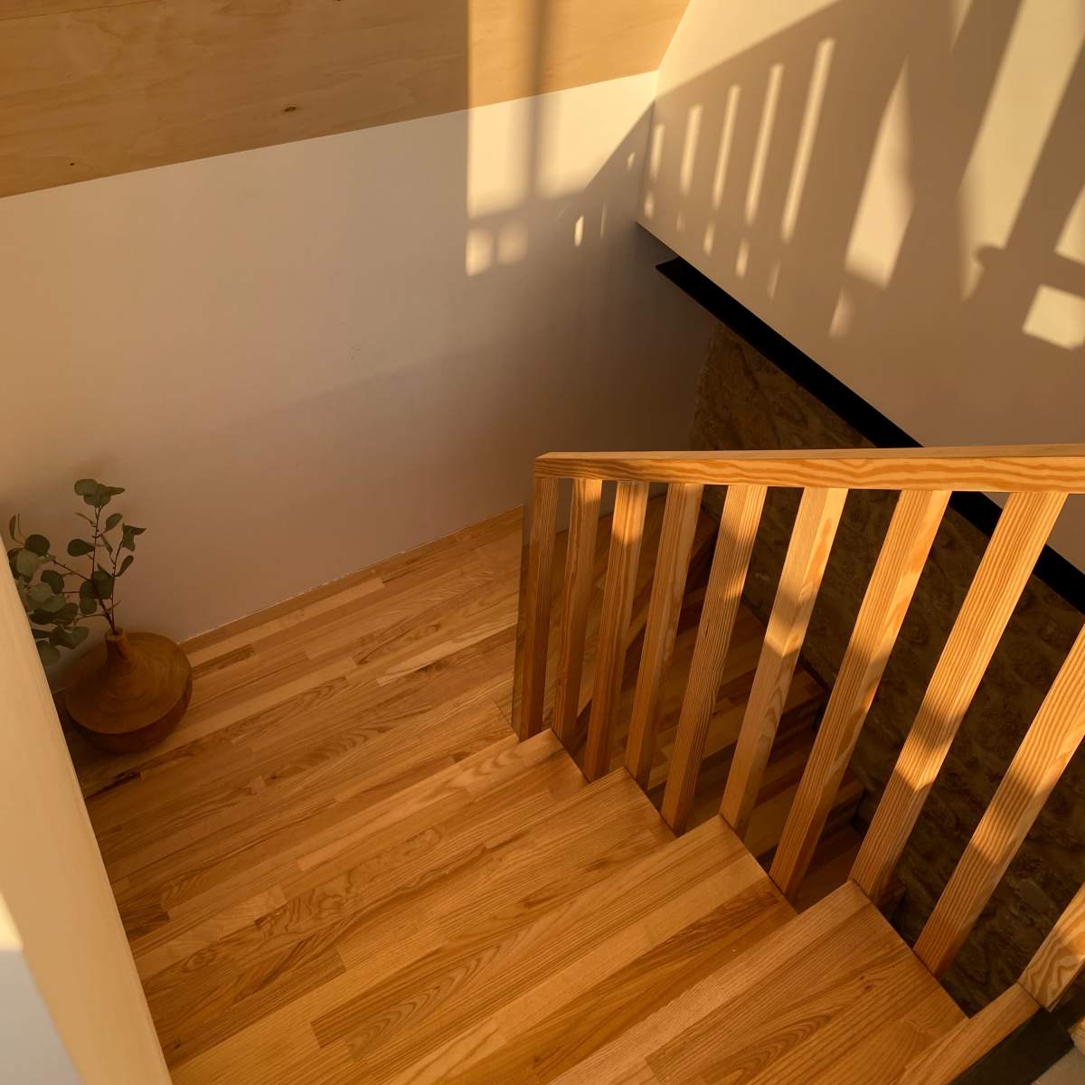 A wooden staircase leads down to a lower level, with sunlight casting shadows on the walls.