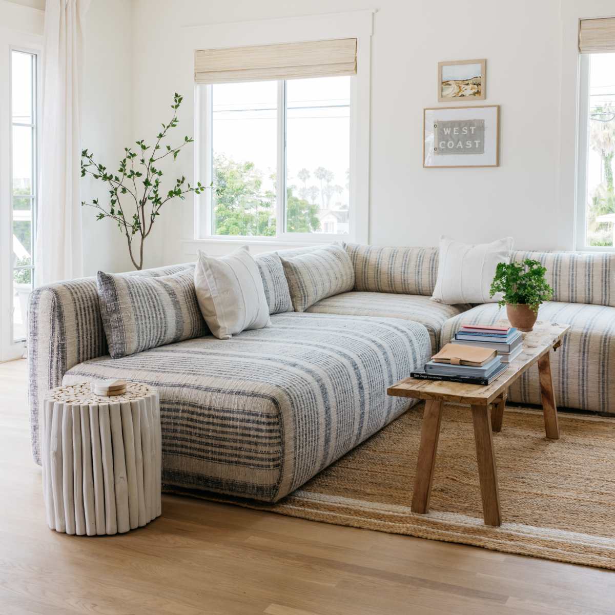 A spacious living room features a light-colored sectional sofa, a wooden coffee table, and natural light filtering through large windows.