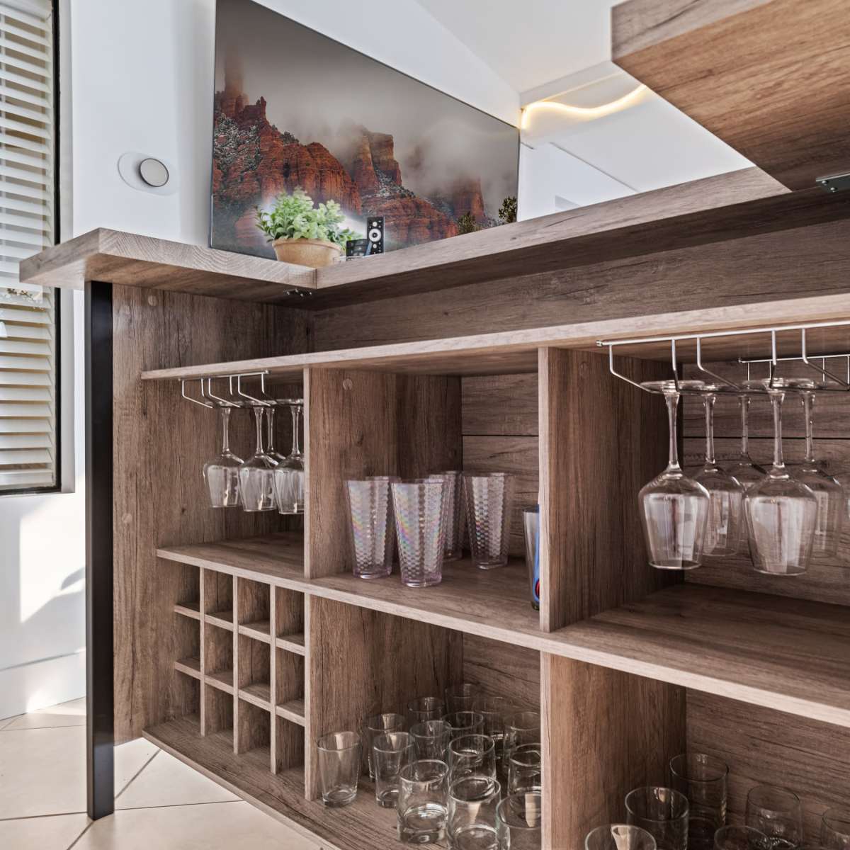 A wooden bar with hanging wine glasses, a storage area for bottles, and a display of clear drinking glasses.