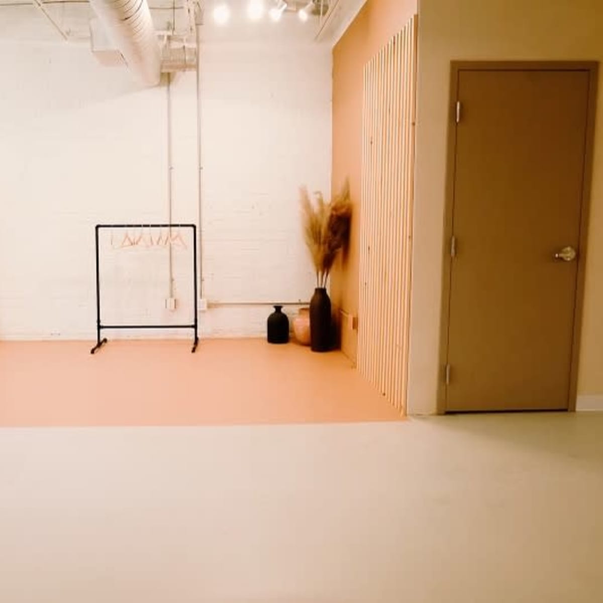 A minimalistic room with a light-colored floor, a clothing rack, vases, and a decorative wall panel.