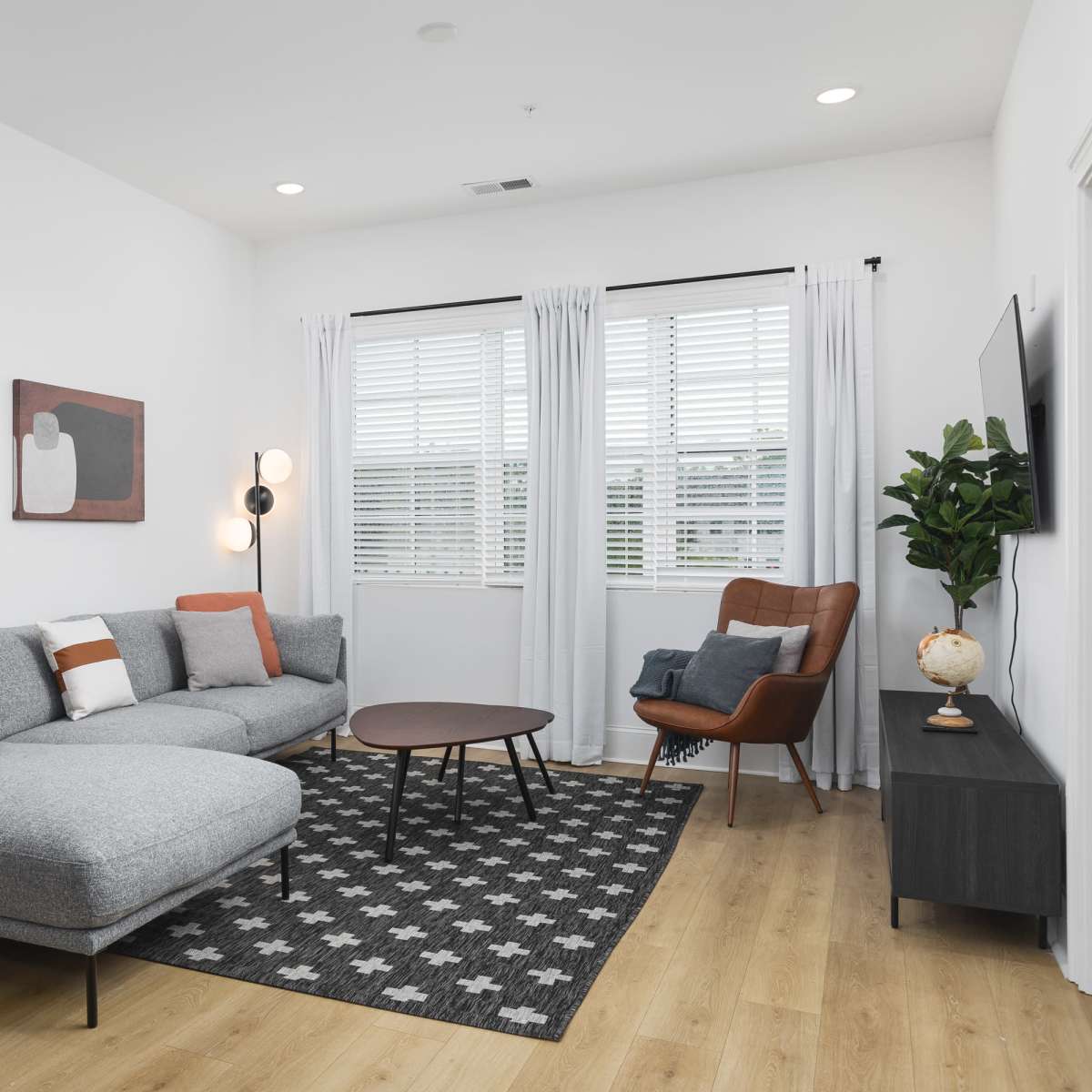 A modern living room featuring a grey sectional sofa, a round coffee table, an armchair, and artwork on the walls, with large windows letting in natural light.