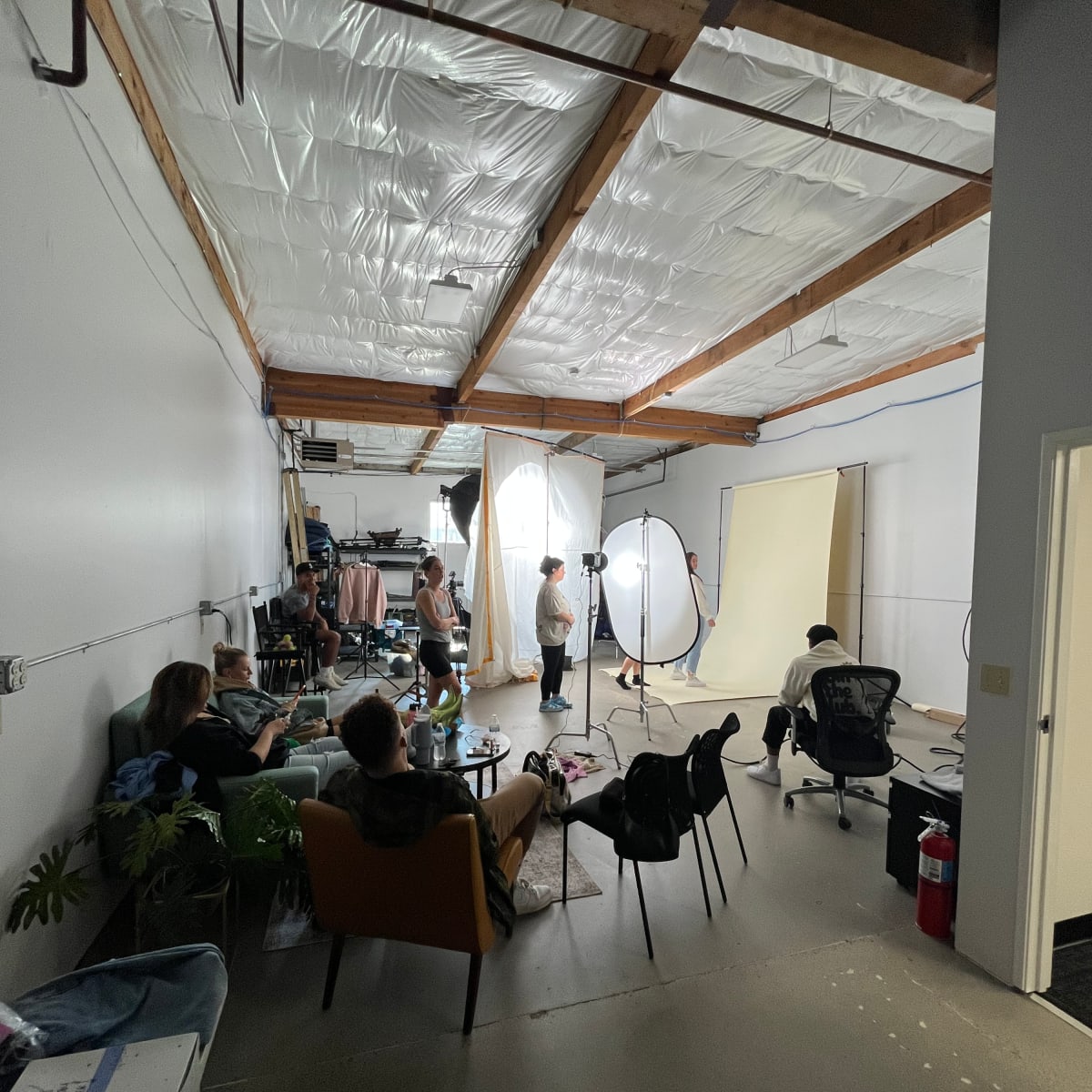 A group of people is gathered in a spacious studio, with photography equipment set up and backdrops arranged for a photoshoot.