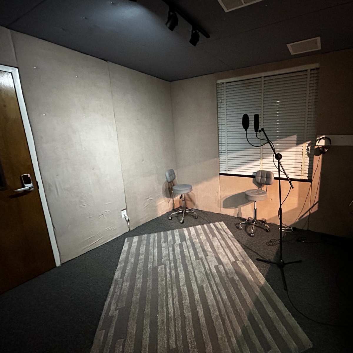 A small recording studio with two chairs, a microphone setup, and a window overlooking another room.