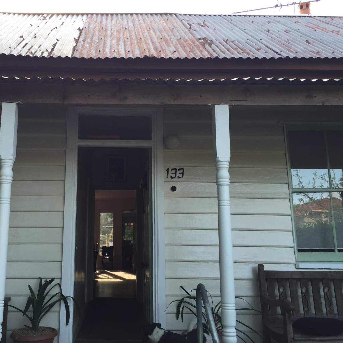 The entrance of a wooden house with a corrugated metal roof and two white pillars supporting the porch.