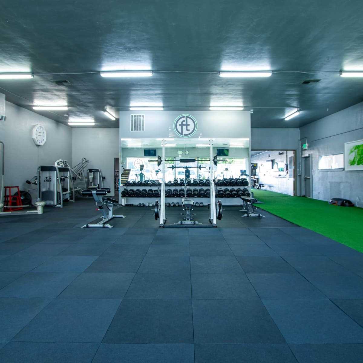 A spacious gym with workout equipment, black rubber flooring, and a green turf area.