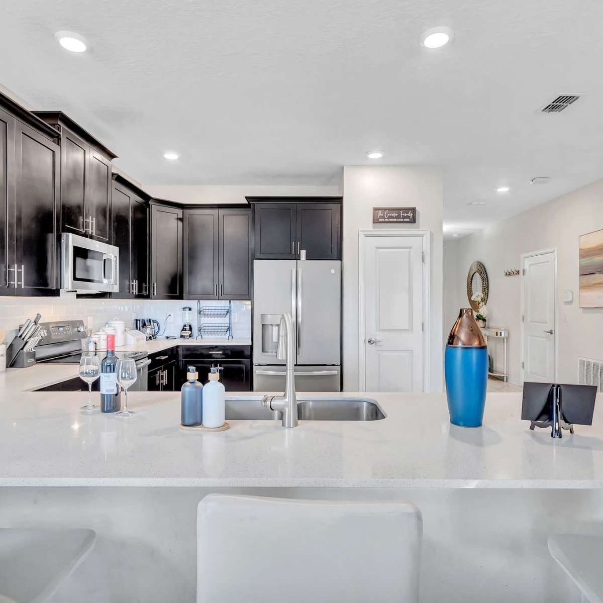 A modern kitchen with dark cabinetry, stainless steel appliances, and a white countertop with bar seating.