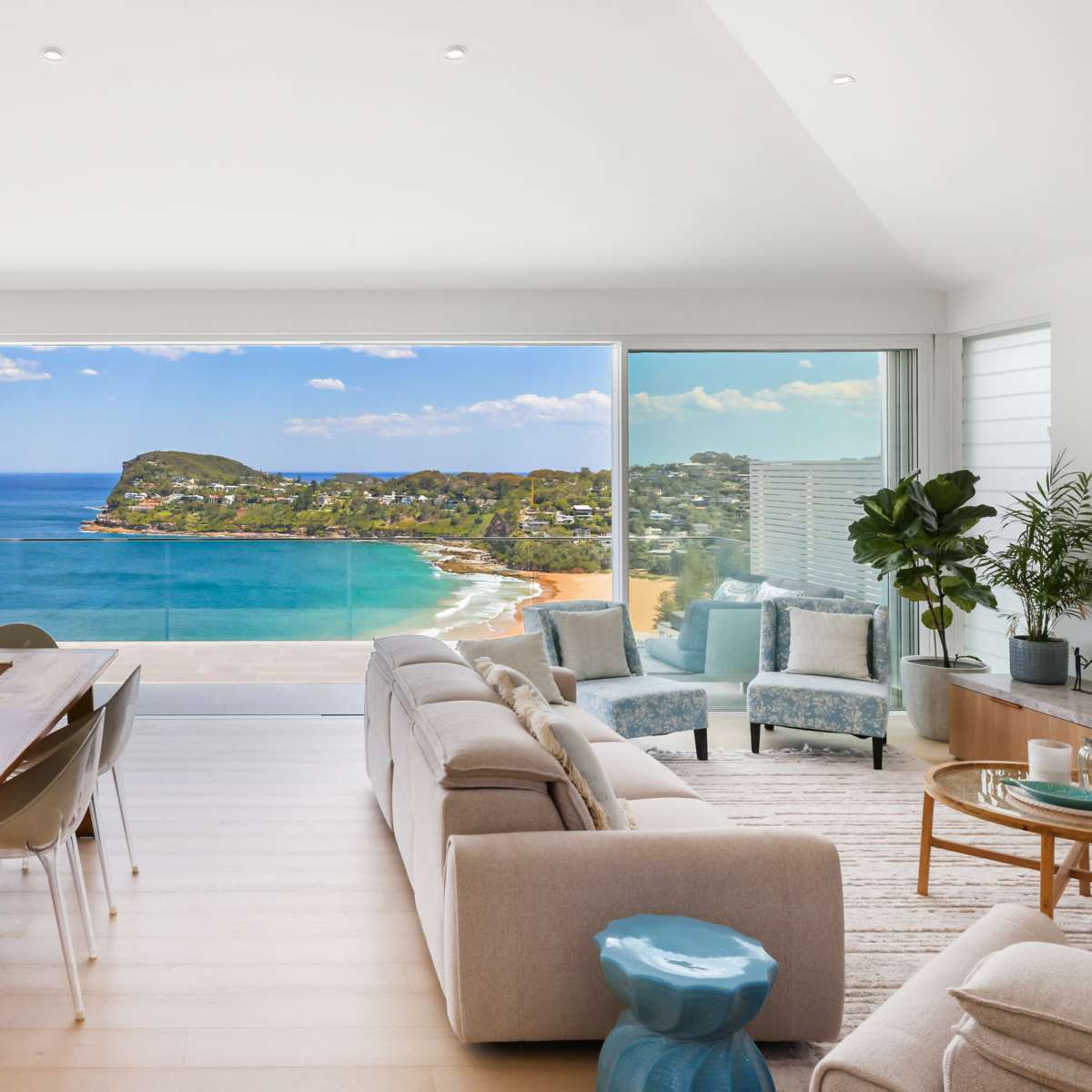 A modern living space with a view of the ocean and a coastal landscape through large glass windows.