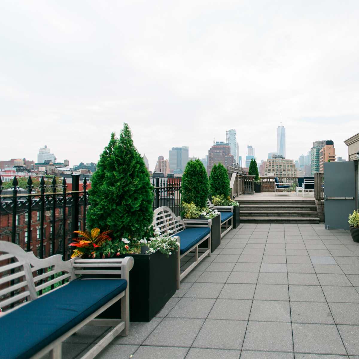 A rooftop terrace features benches with potted plants and a view of city skyscrapers in the distance.