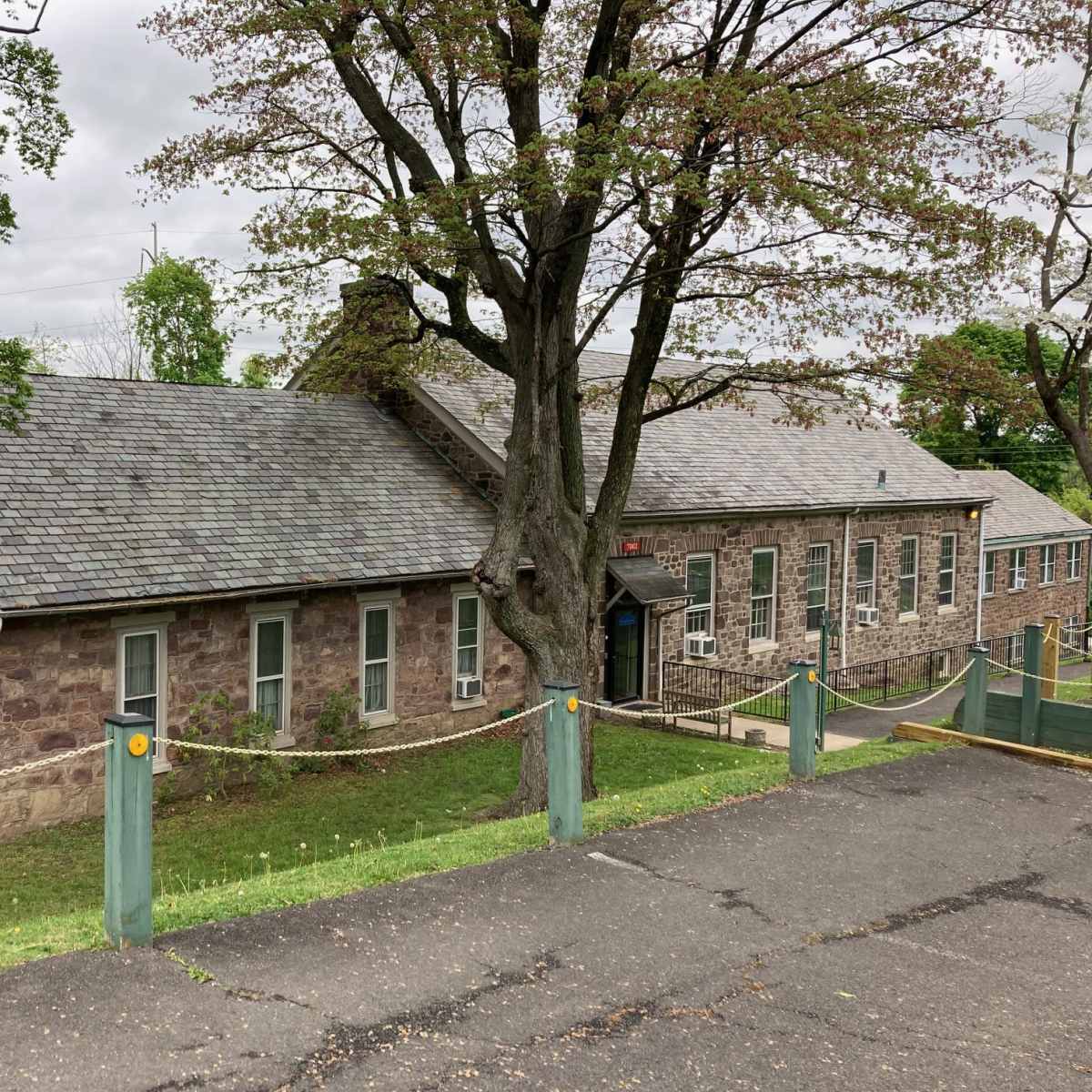 A stone building with a sloped roof, surrounded by green grass and trees, located on a hillside.