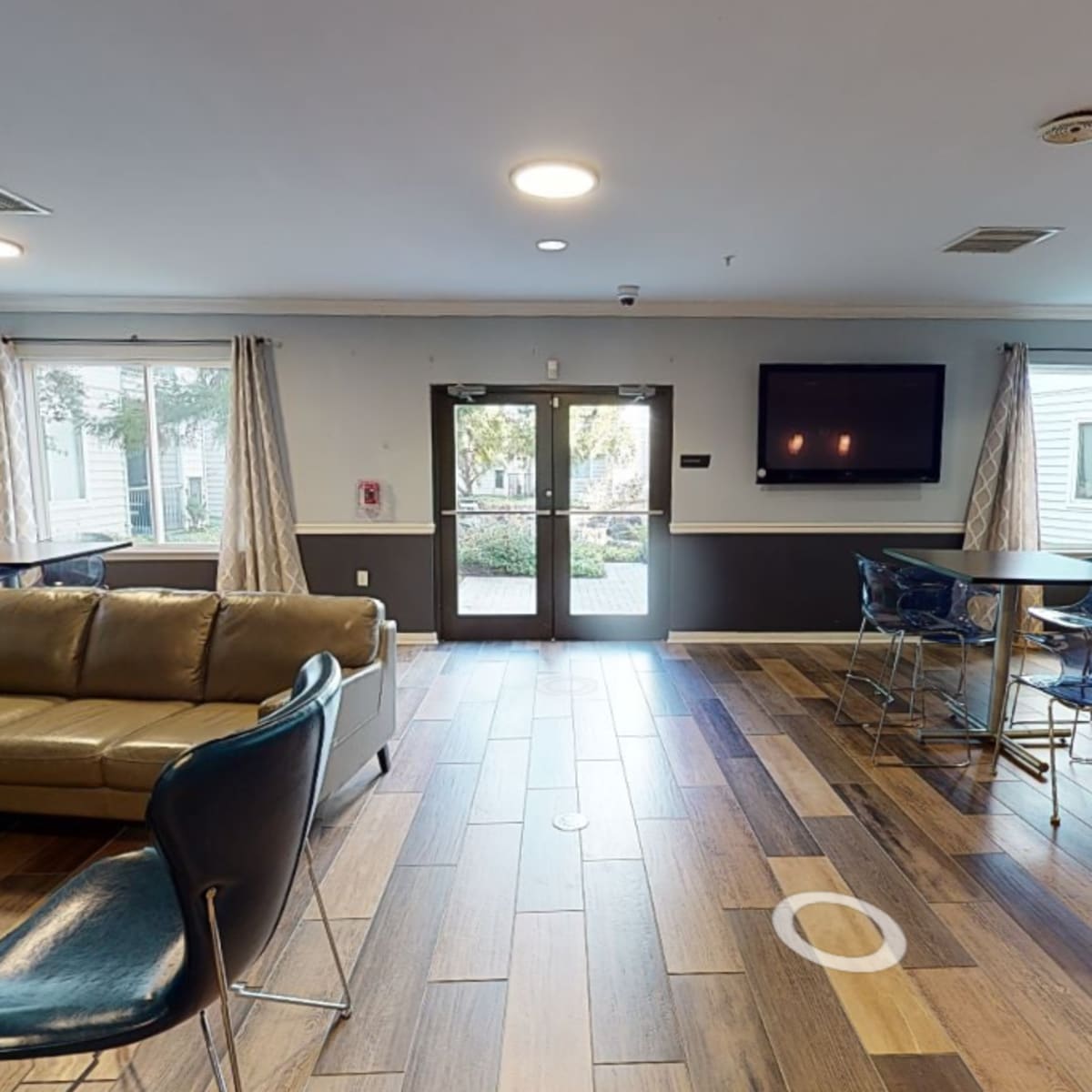 A spacious communal area with a sofa, dining tables, and large windows allowing natural light.