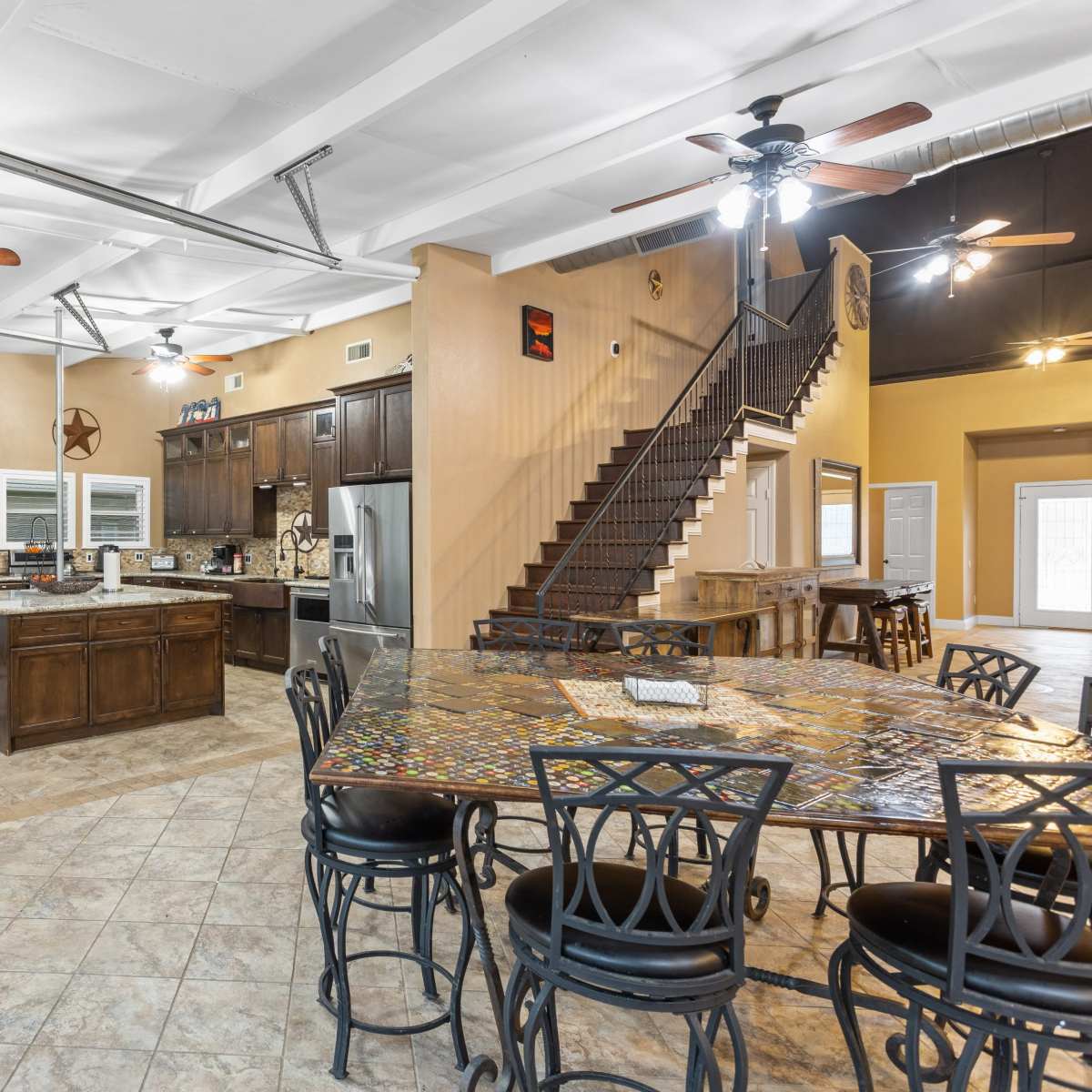 A spacious, open-concept kitchen and dining area with a large table, modern appliances, and a staircase leading to an upper level.