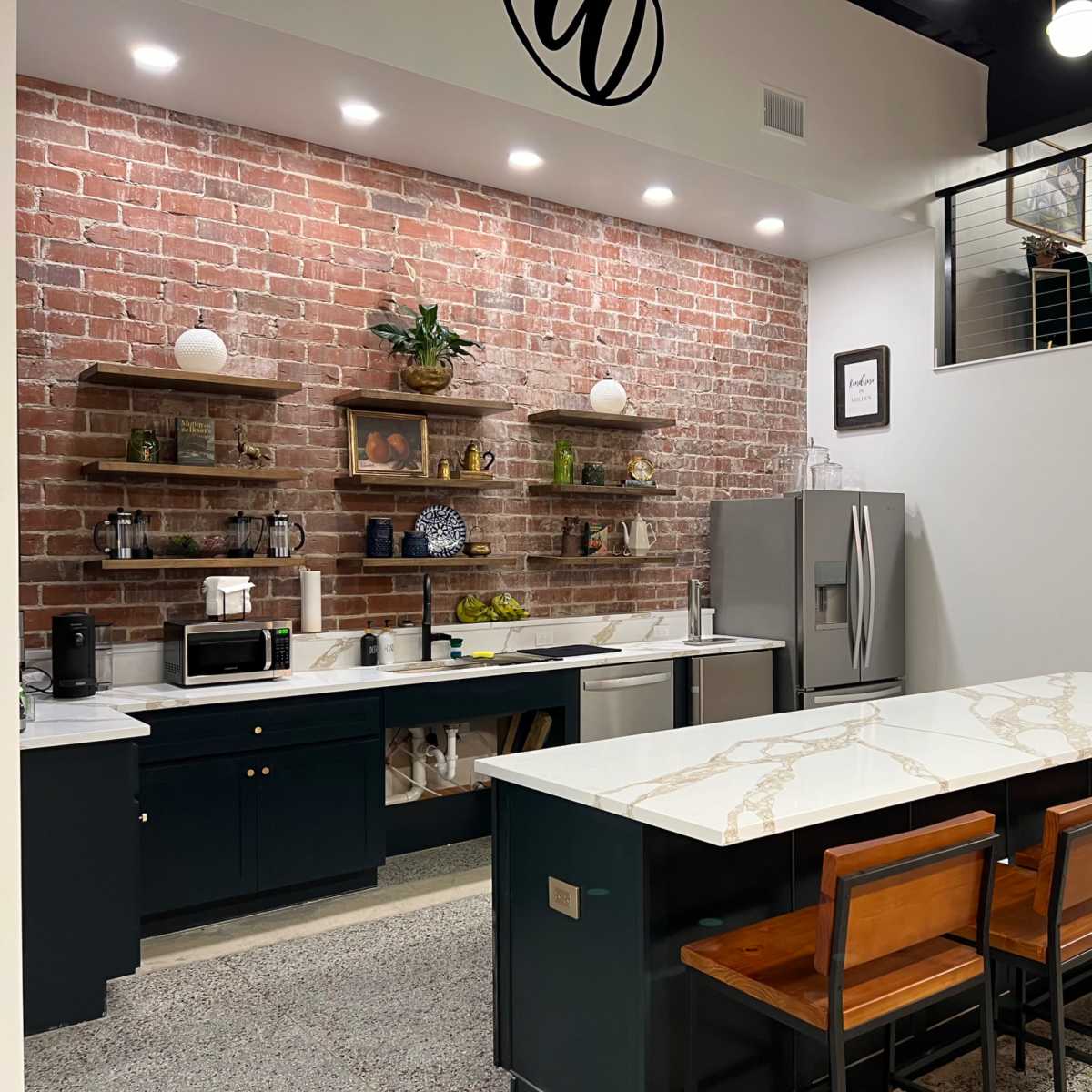 A modern kitchen with a brick wall, dark cabinetry, and a large island with a marble countertop and bar stools.