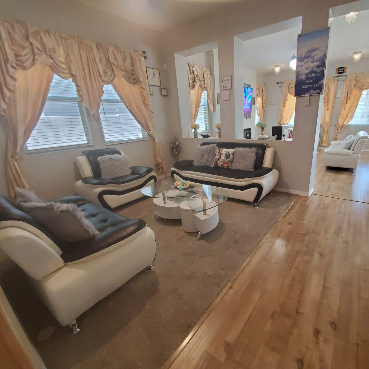 A modern living room with a beige rug, white and black sofas, decorative curtains, and a glass coffee table.