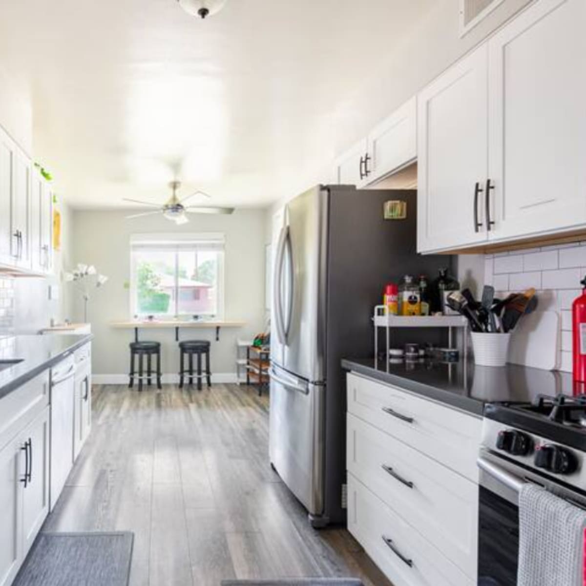A modern kitchen featuring white cabinetry, stainless steel appliances, and a breakfast bar with two stools.