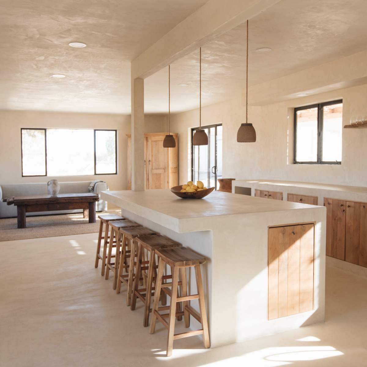 A spacious, modern kitchen features a large island with wooden stools and minimalist cabinetry, illuminated by natural light from multiple windows.