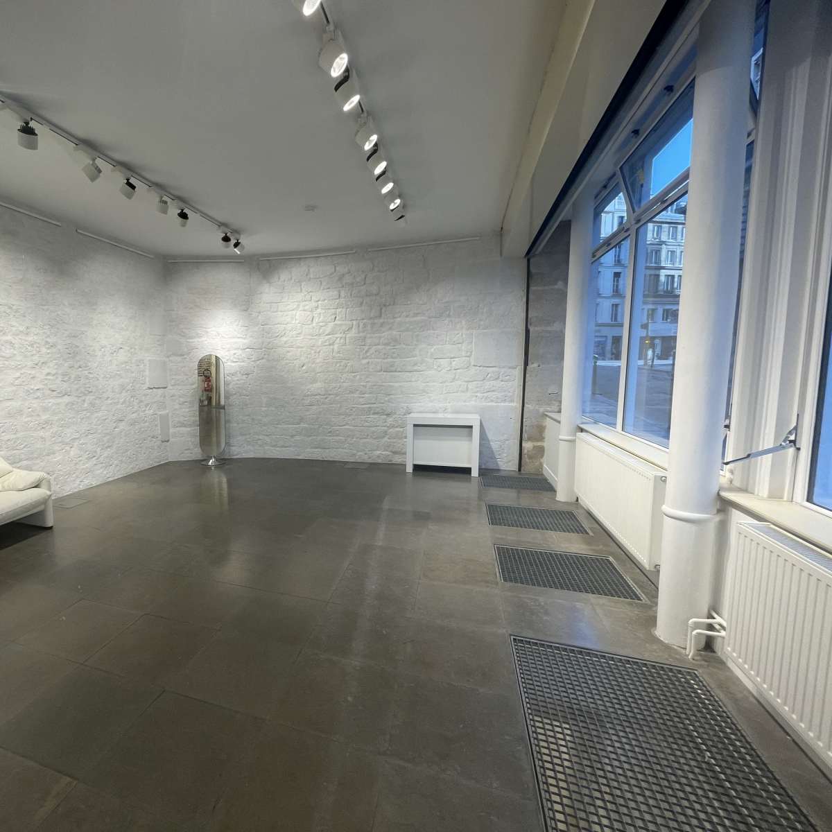 A spacious, empty room with a white couch, a side table, and large windows allowing natural light to enter.
