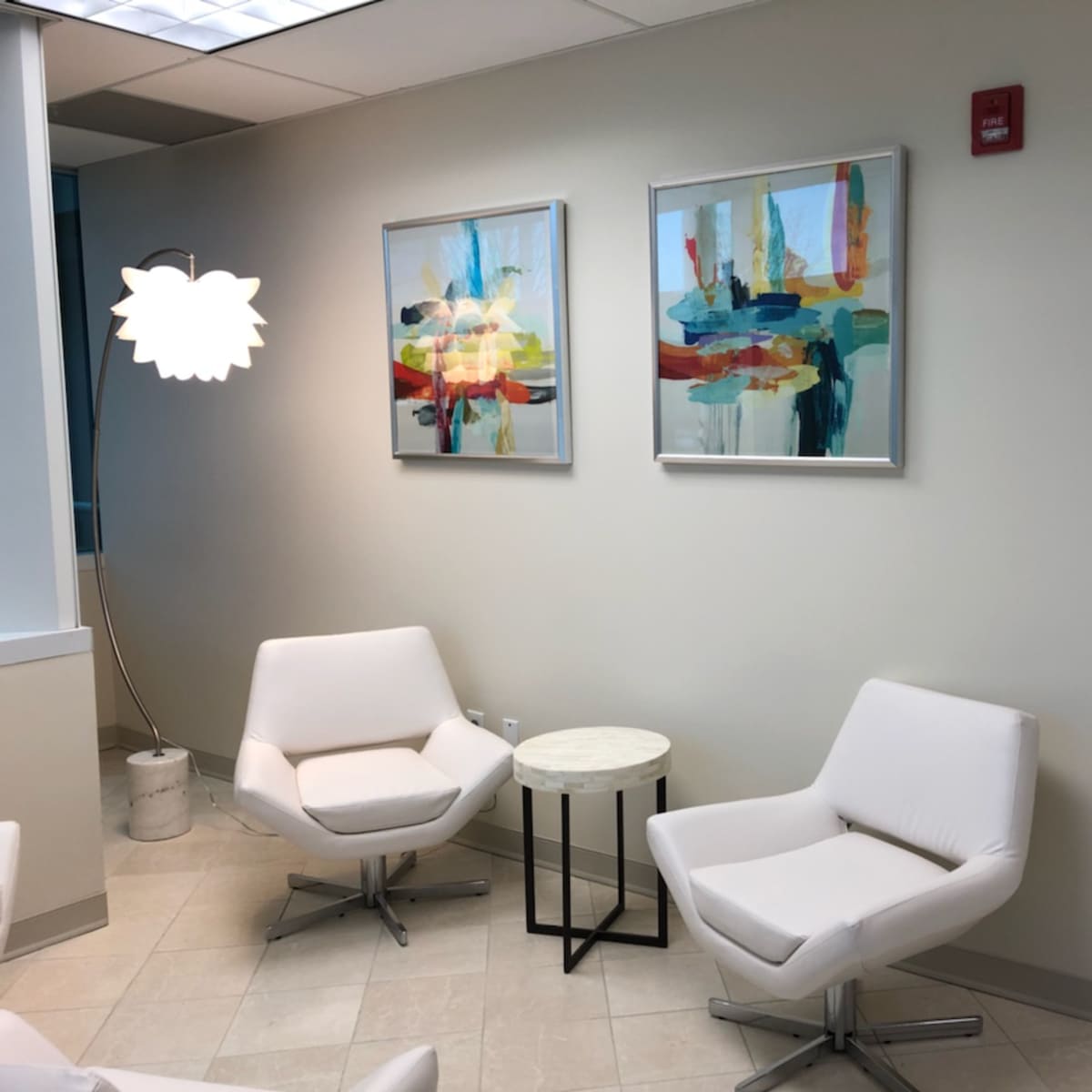 A modern waiting area with two white chairs, a small round table, and abstract artwork on the walls.