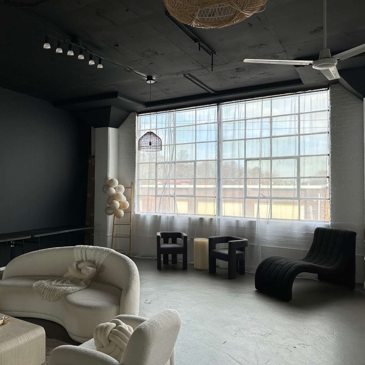 A modern, minimalist interior with a large window, a black accent wall, and various seating arrangements including a white sofa and black chairs.