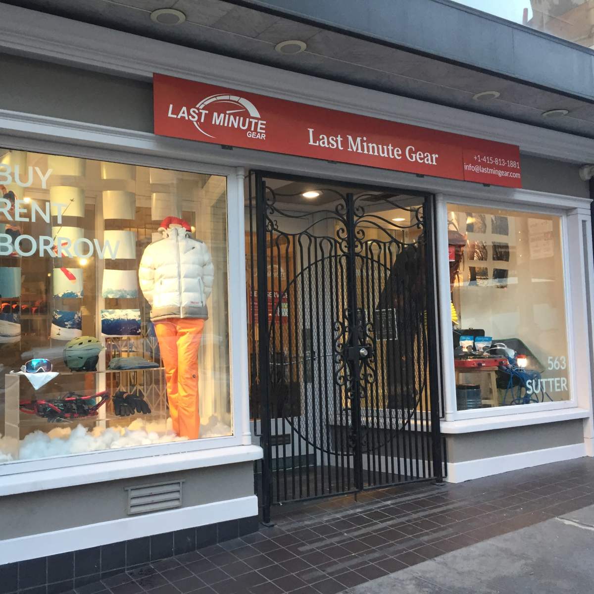 The storefront of "Last Minute Gear" features a window display showcasing winter apparel and equipment, with a sign highlighting options to buy, rent, or borrow.