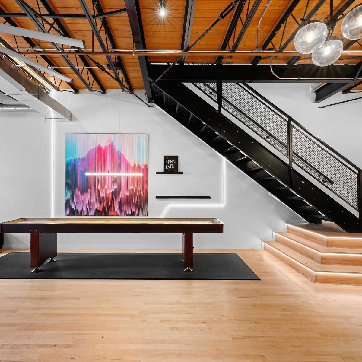A modern interior space featuring a pool table, a staircase with black railings, and colorful artwork on the wall.