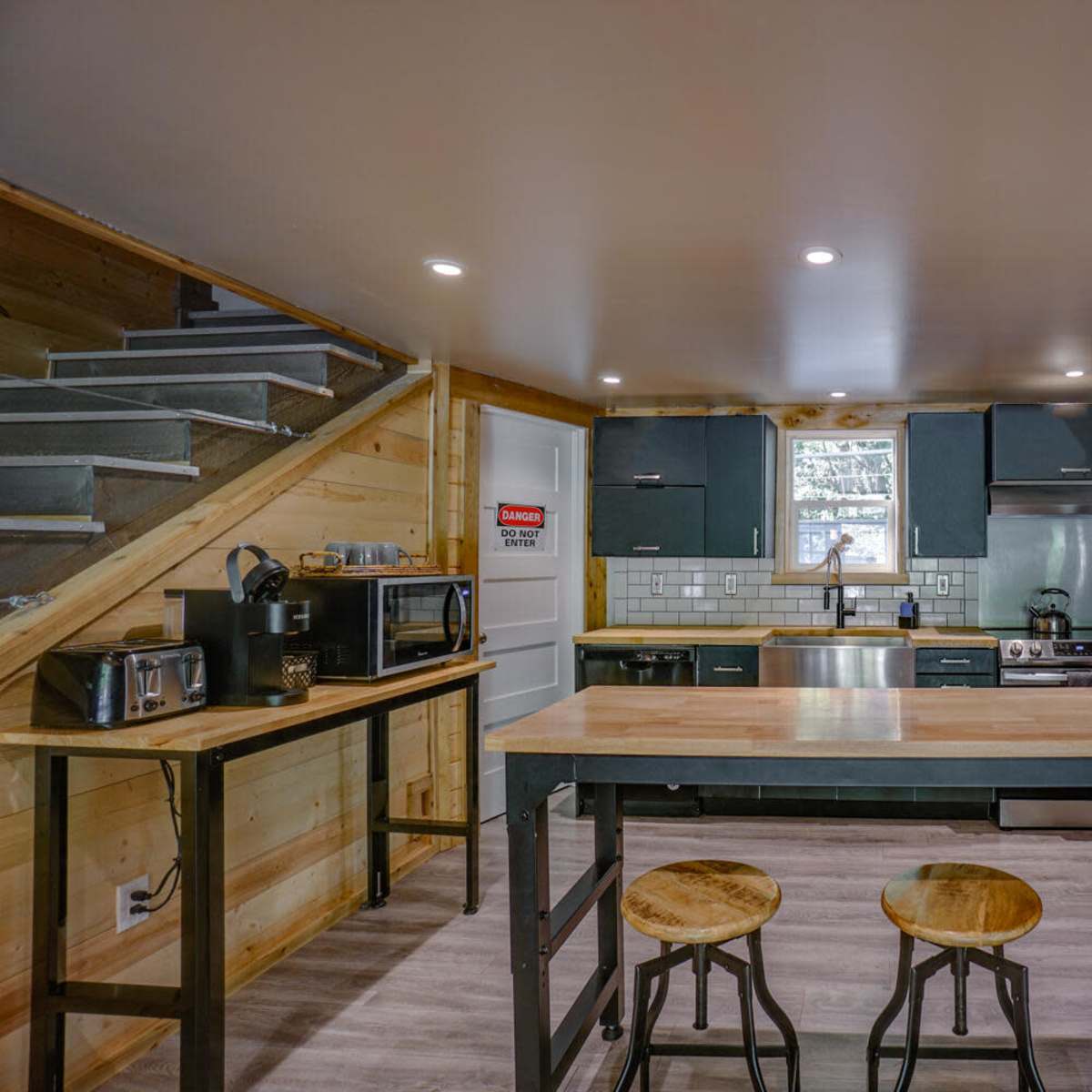 A modern kitchen with wood and metal accents, featuring a central island with stools, stainless steel appliances, and wooden cabinetry.