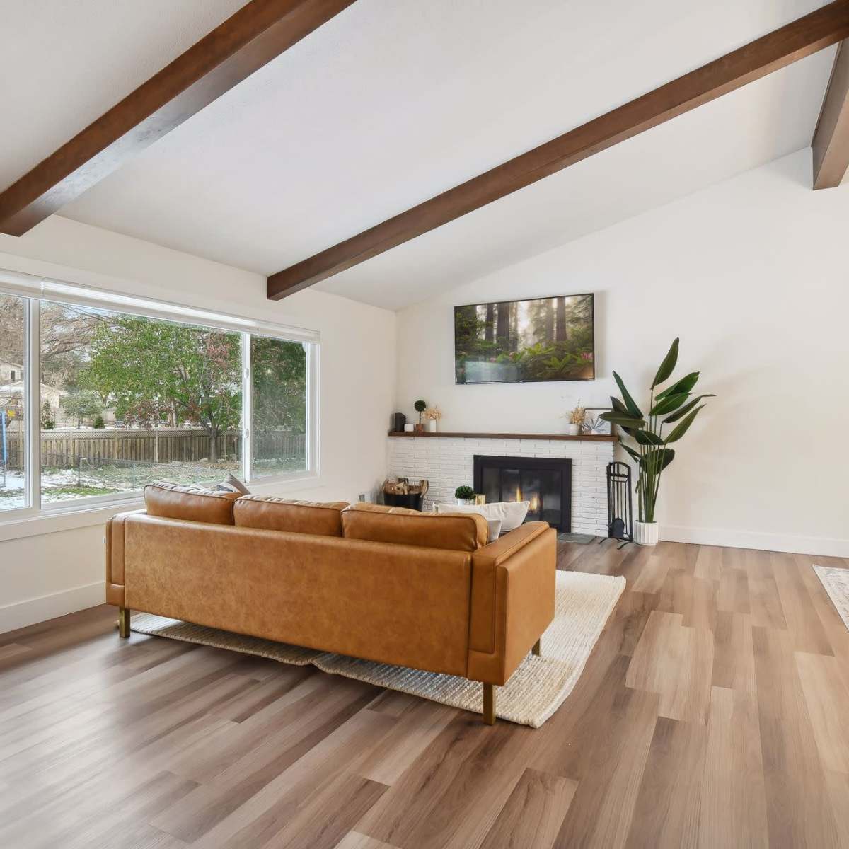 A modern living room with a brown leather sofa, a fireplace, and large windows overlooking a snowy outdoor scene.