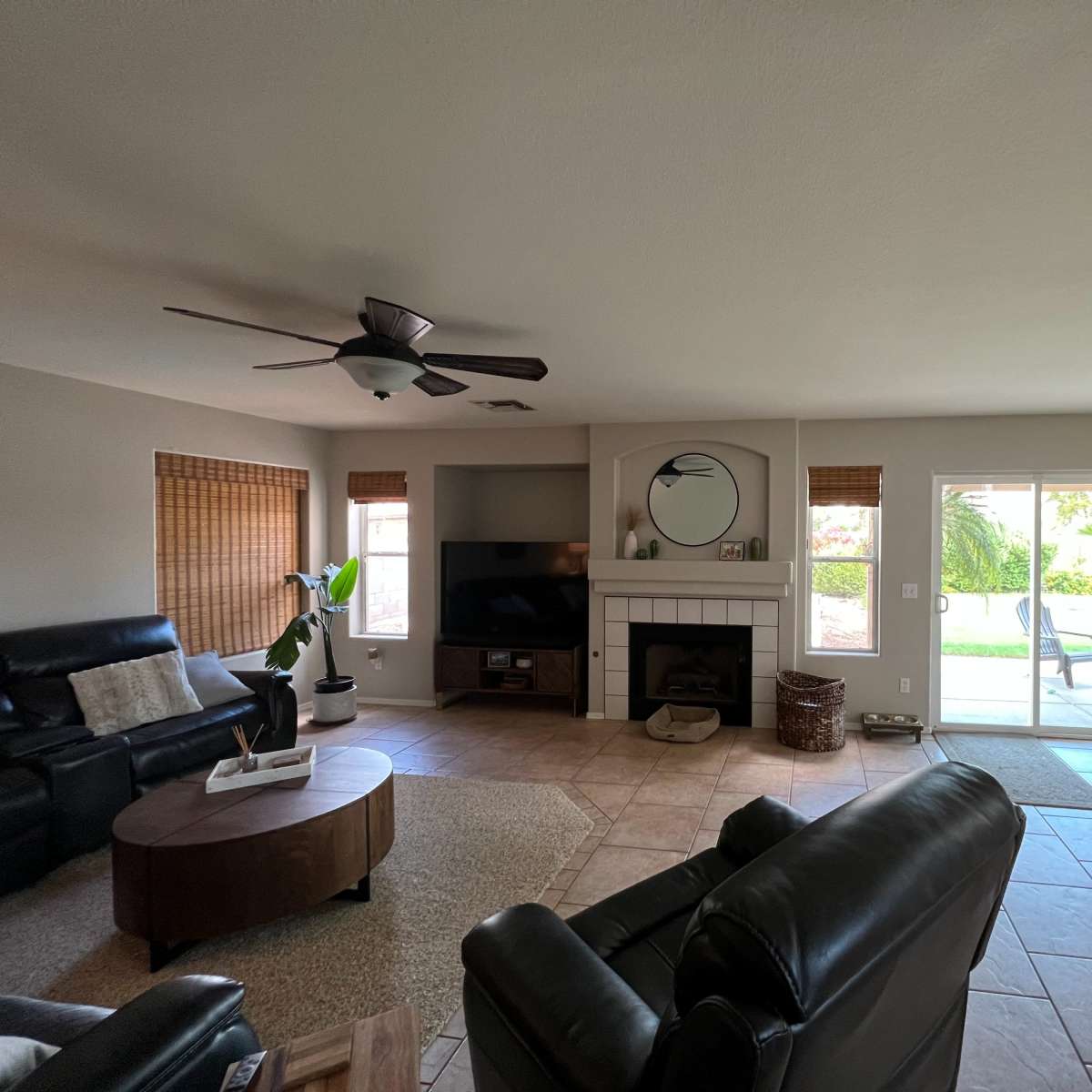 The living room features a seating area with black leather chairs, a round coffee table, a TV unit, and sliding glass doors leading to an outdoor space.