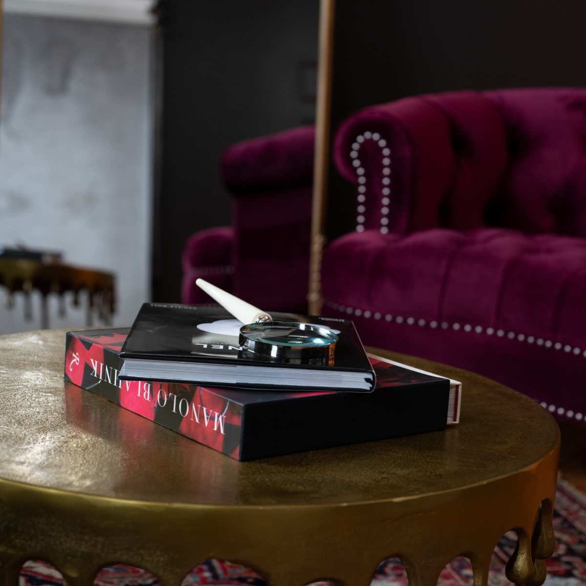 A plush purple tufted couch is set against a dark wall, with a gold coffee table displaying a book and accessories.
