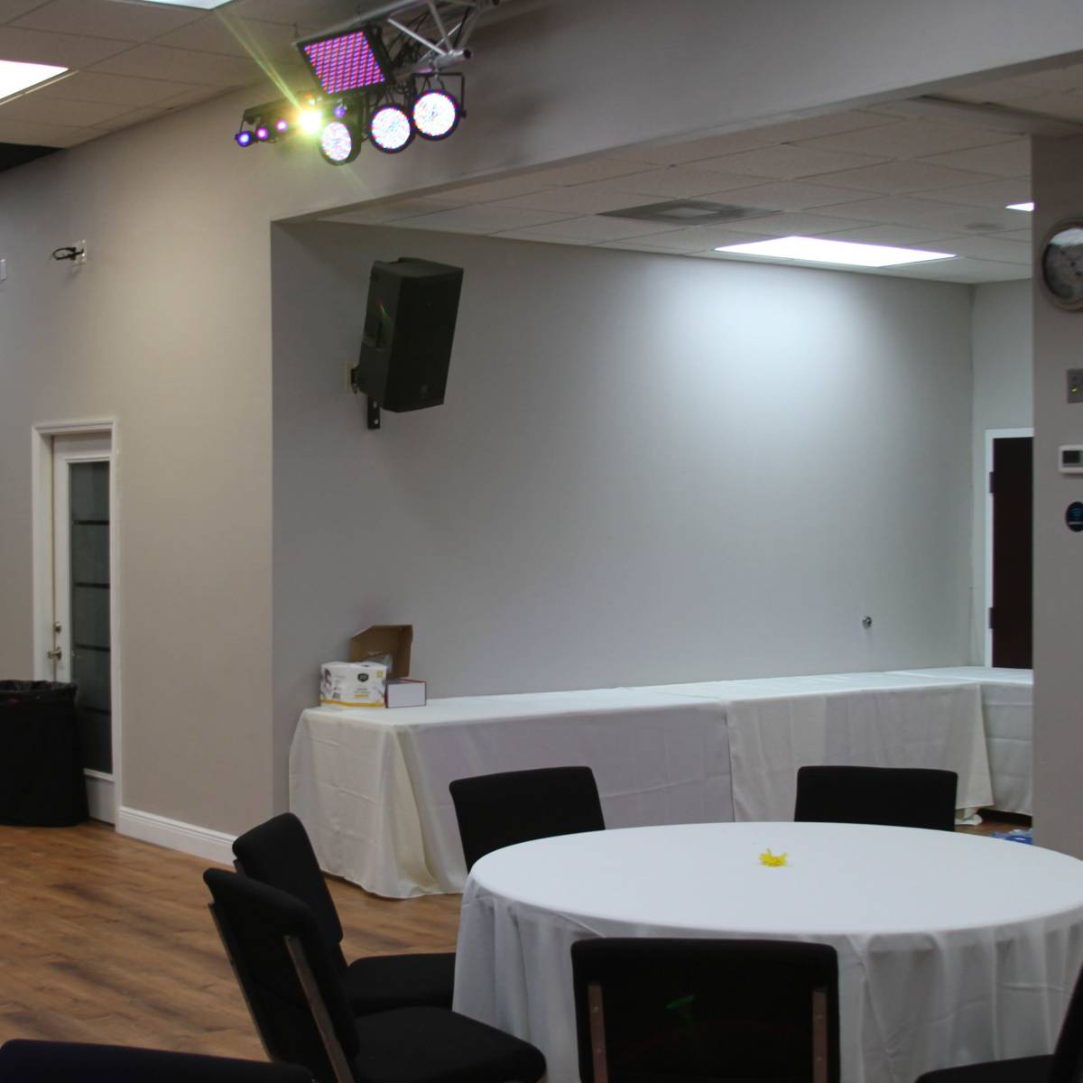 A spacious indoor event space with a round table set up and a stage area featuring lighting and a speaker.