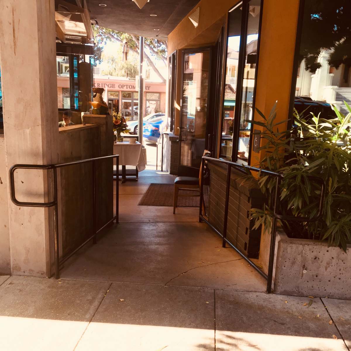 The entrance to a café, featuring an open door with a welcoming interior view and planters on the side of the walkway.