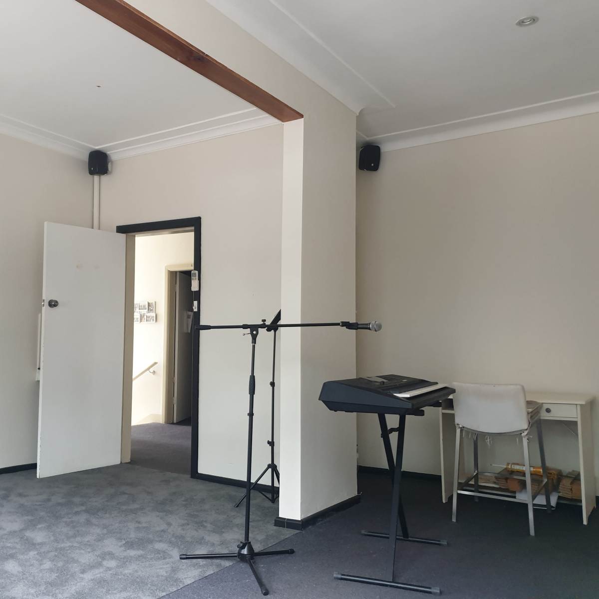 A small room features a doorway, a keyboard on a stand, a microphone, and a whiteboard mounted on the wall.