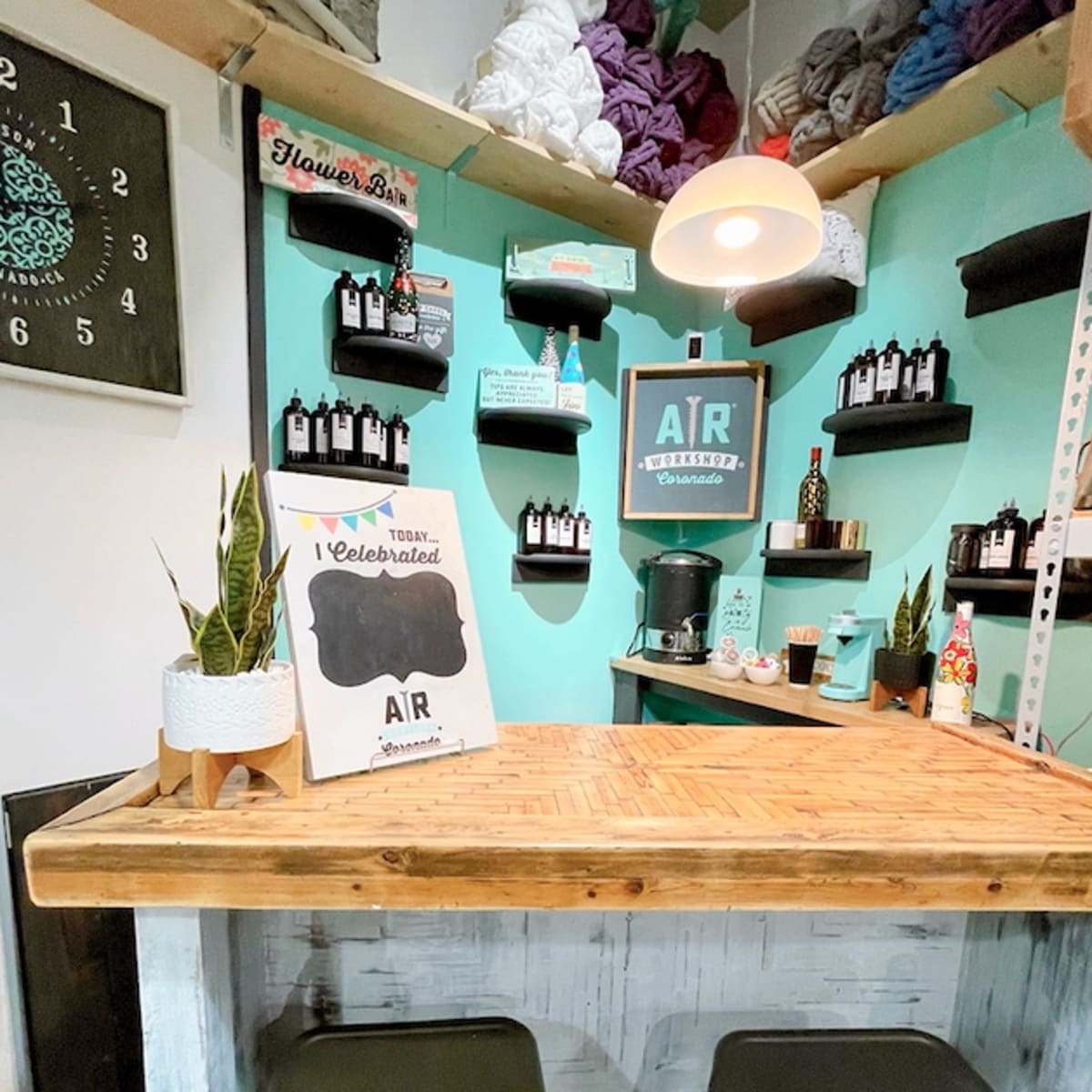 A cozy, well-organized space with a wooden counter, shelves displaying various bottles and decorative items, and a coffee maker against a mint green wall.