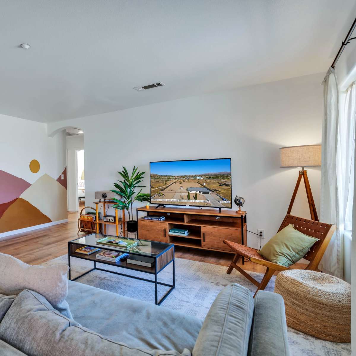 A living room features a modern couch, a television on a wooden console, and a mural of mountains and celestial shapes on one wall.