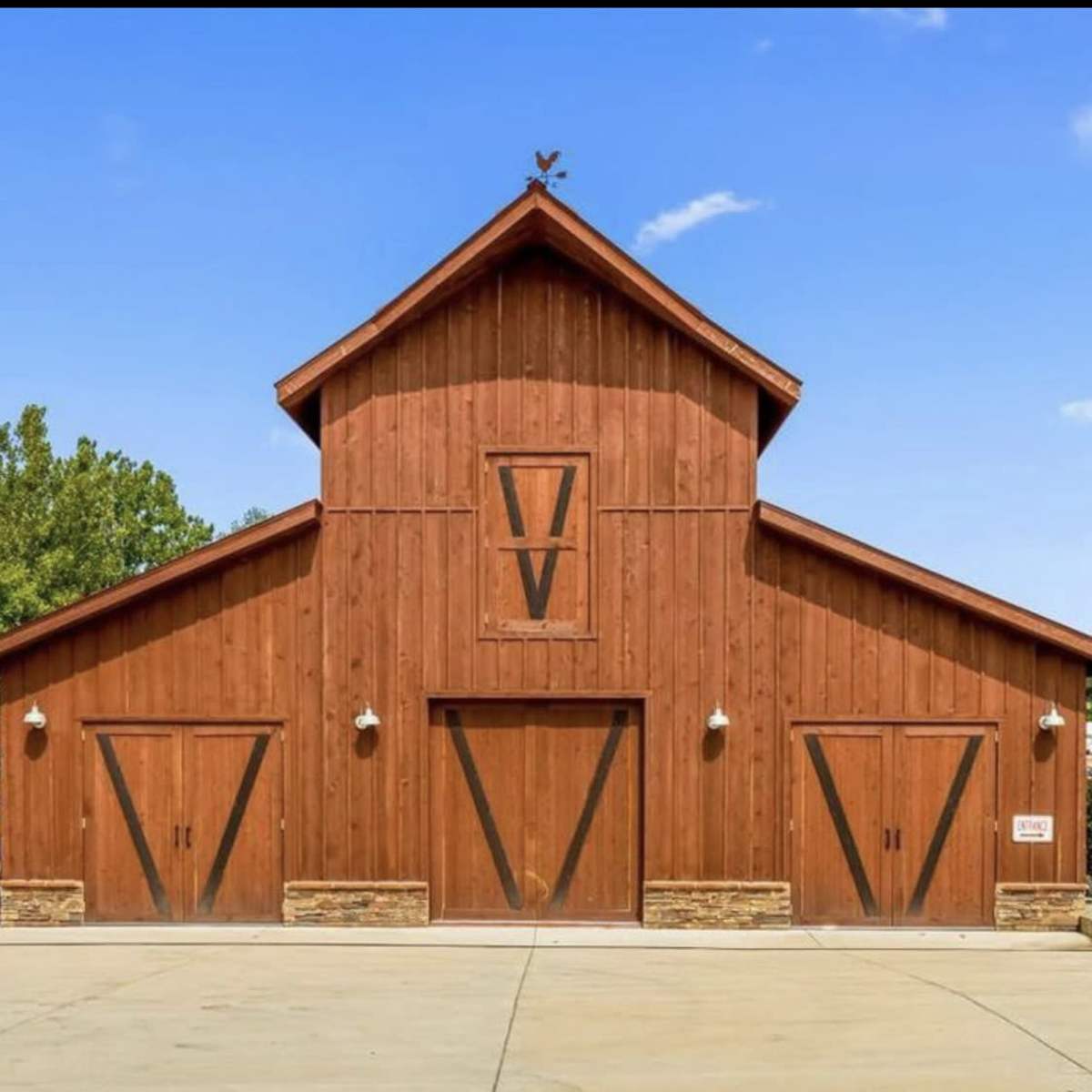 A large wooden barn with a steeply pitched roof, featuring two large double doors and a weather vane on top.