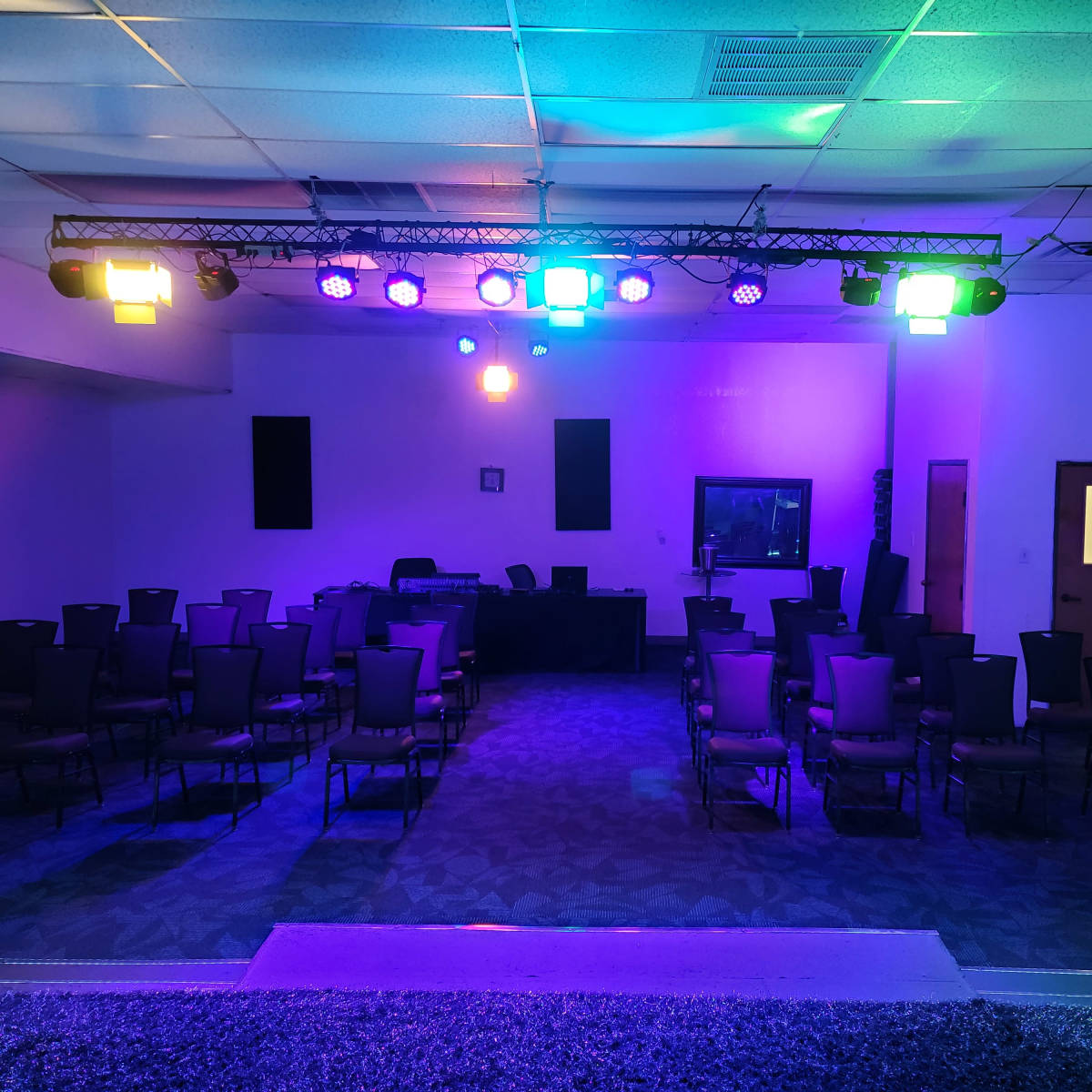 An empty conference room features rows of chairs facing a stage with colorful lighting.