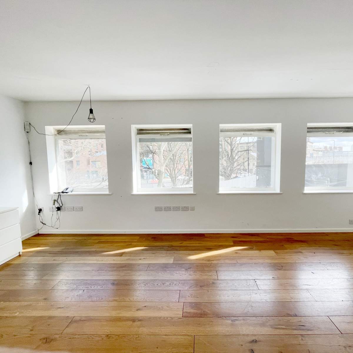 An empty room with hardwood floors and four windows providing natural light.